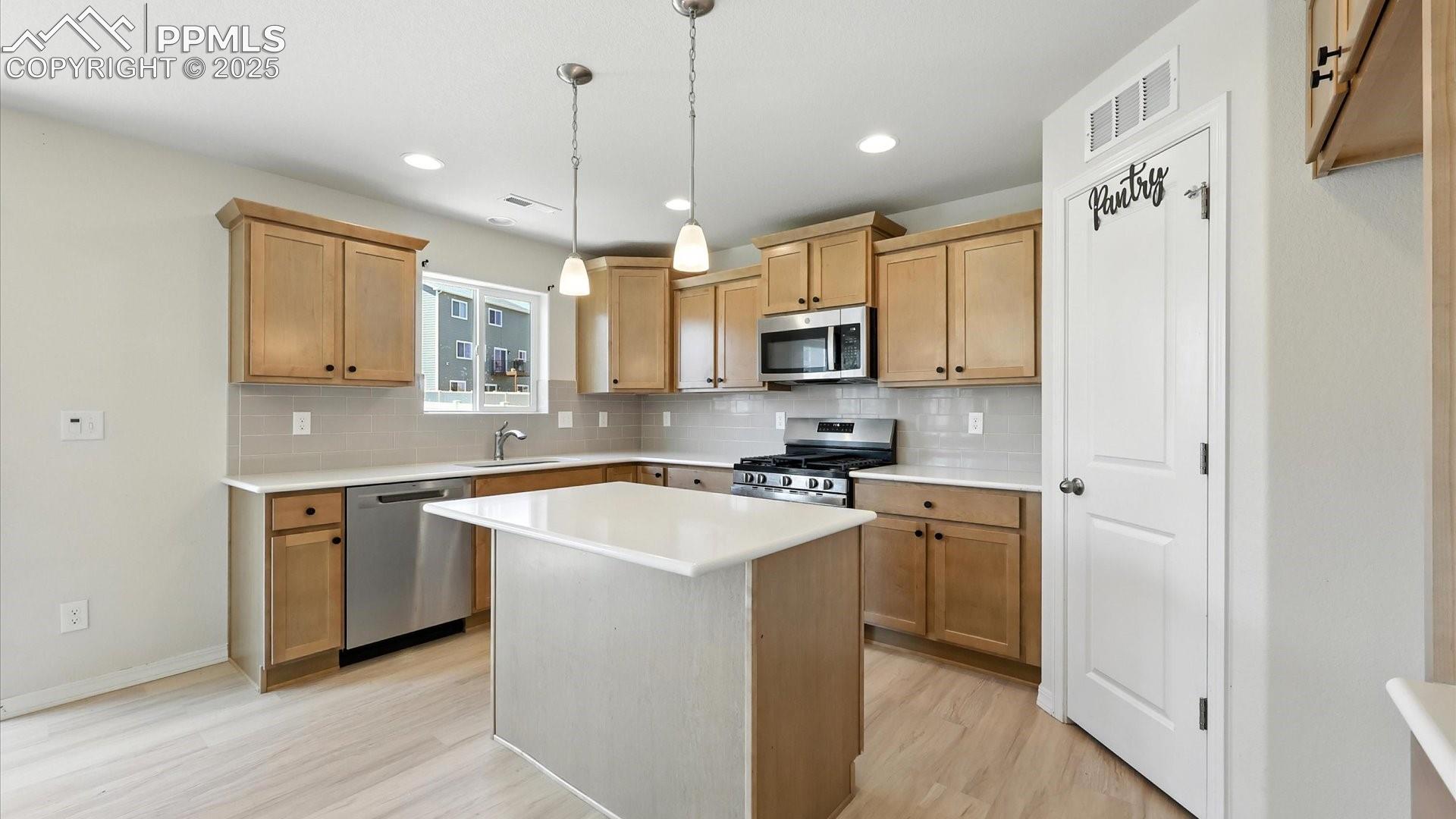 Island Kitchen with breakfast bar, pantry, and stainless steel appliances including a gas range oven, microwave, and dishwasher.