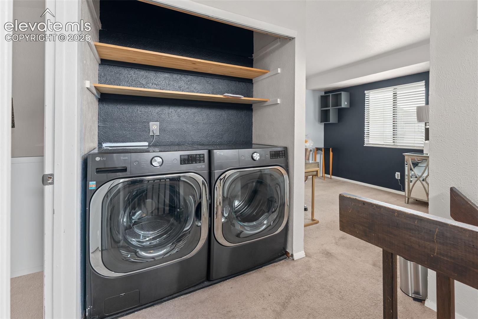 Dedicated laundry area with built-in shelving, front-load washer and dryer, and dark accent wall