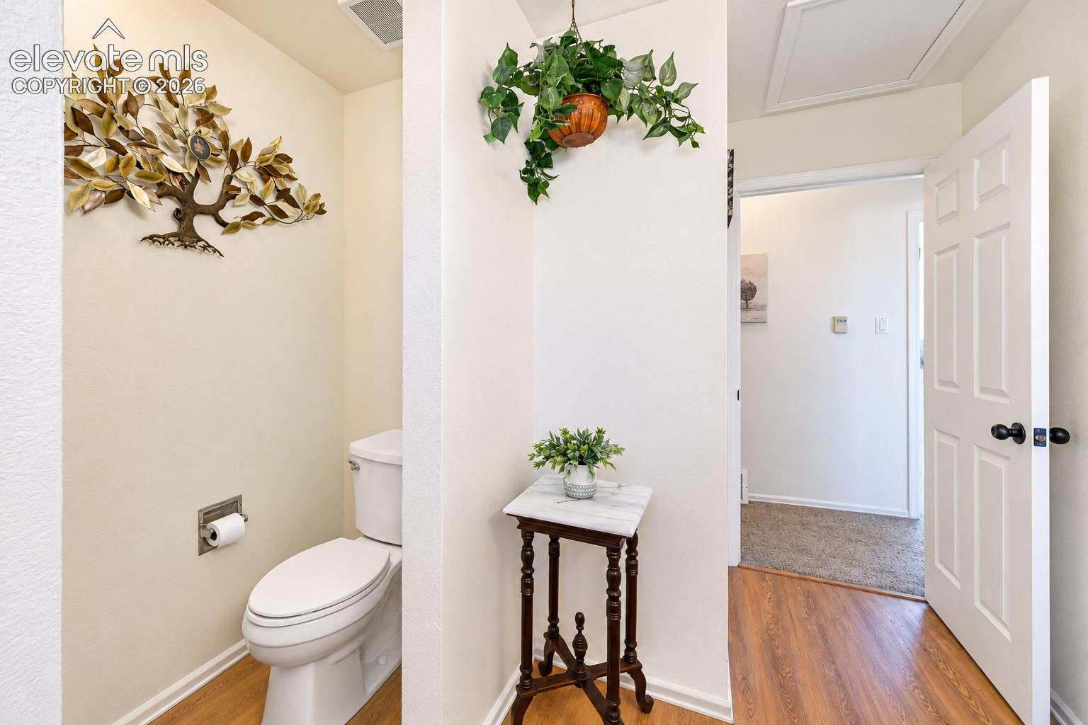 Full bathroom featuring a standard height toilet, six-panel interior door, and wood-finish flooring