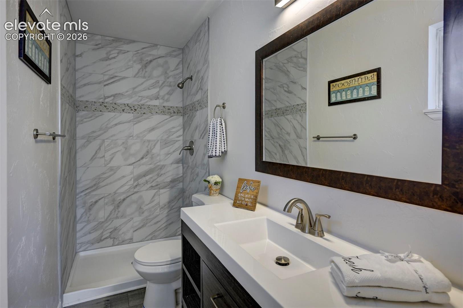 Bathroom featuring a vanity with a white countertop and rectangular undermount sink, large framed wall mirror, and walk-in shower with stone-patterned tile surround and accent inlay