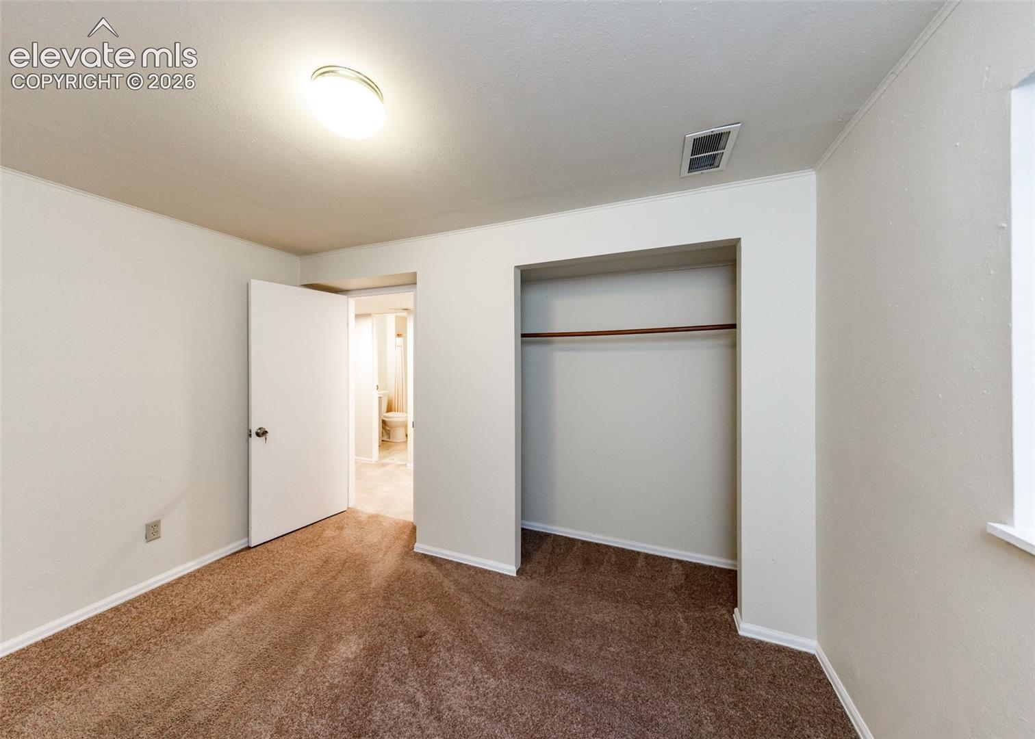 Neutral wall paint, wall-to-wall carpeting, and a built-in closet with an installed rod