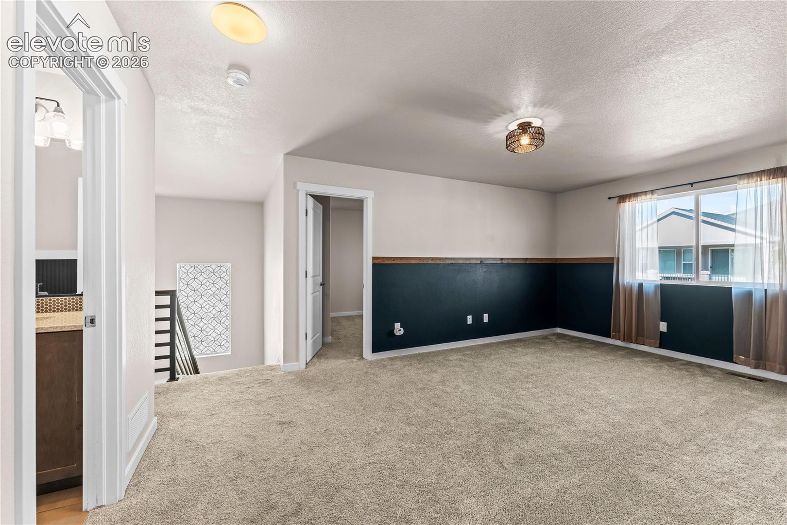 Neutral carpeted flooring, decorative wainscoting with dark-toned paint, two flush-mount light fixtures, and a dual-pane window