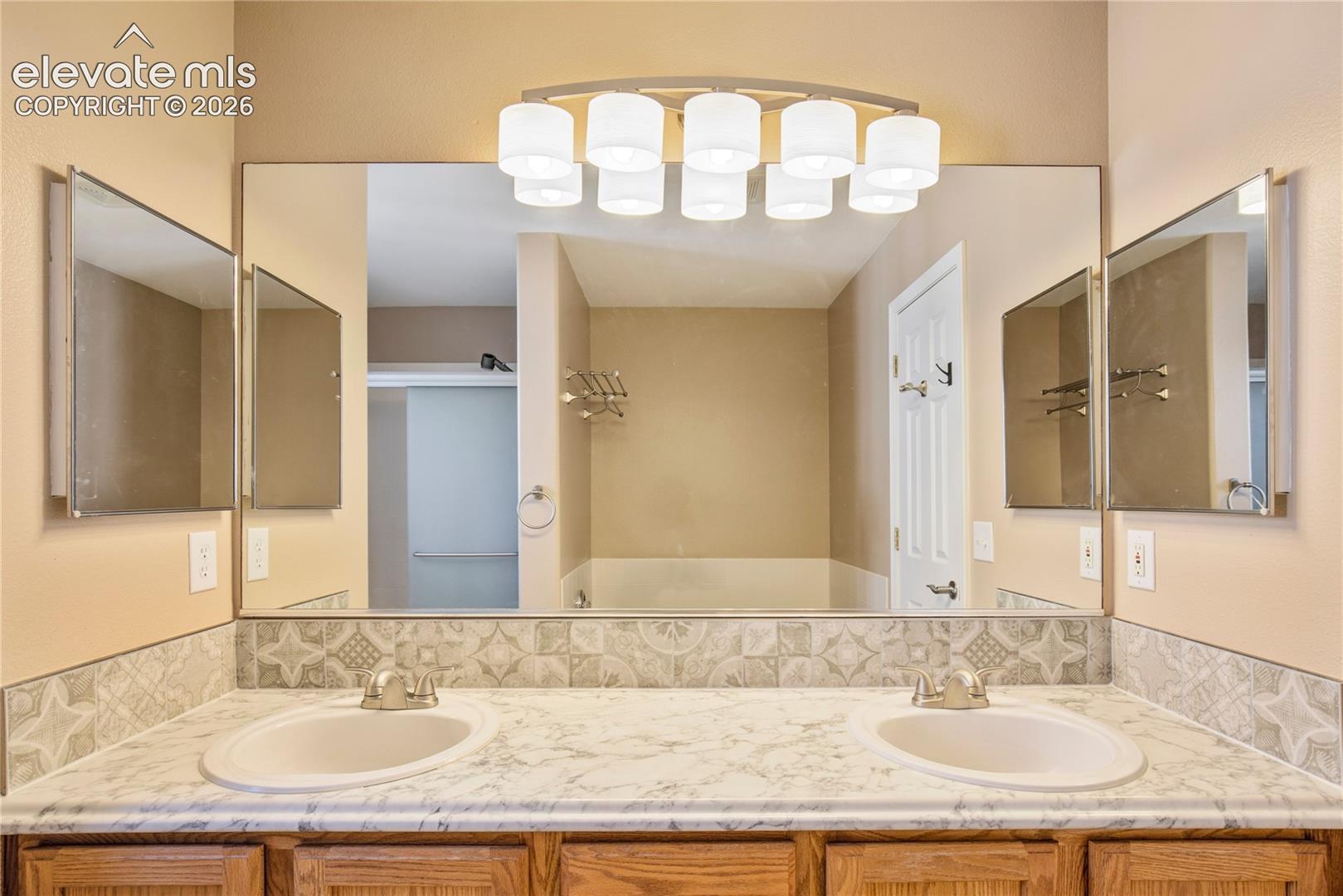 Two sinks, expansive mirrors + overhead vanity lighting provide plenty of practical space, with convenient access to the primary suite's walk-in closet.