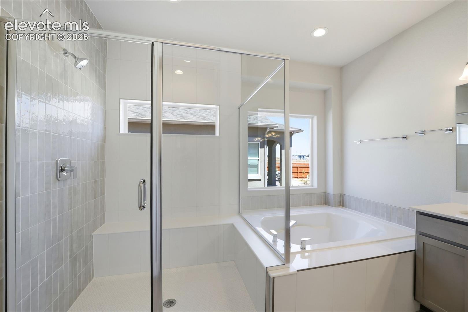 Walk-in shower featuring vertically stacked tile walls and a built-in bench, paired with a soaking tub encased in matching tile, glass shower enclosure, and vanity with stone-surface countertop