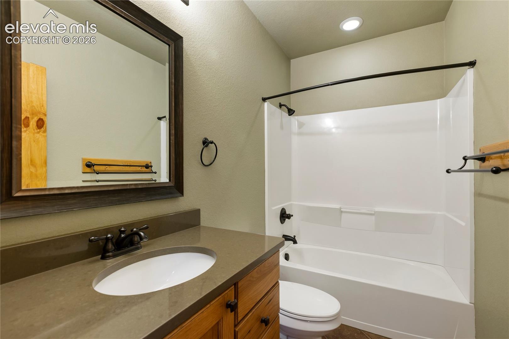 Bathroom featuring a wood vanity with a solid surface countertop, an integrated sink with a dual-handle faucet, a framed mirror, and a tub-shower combination with matte black hardware