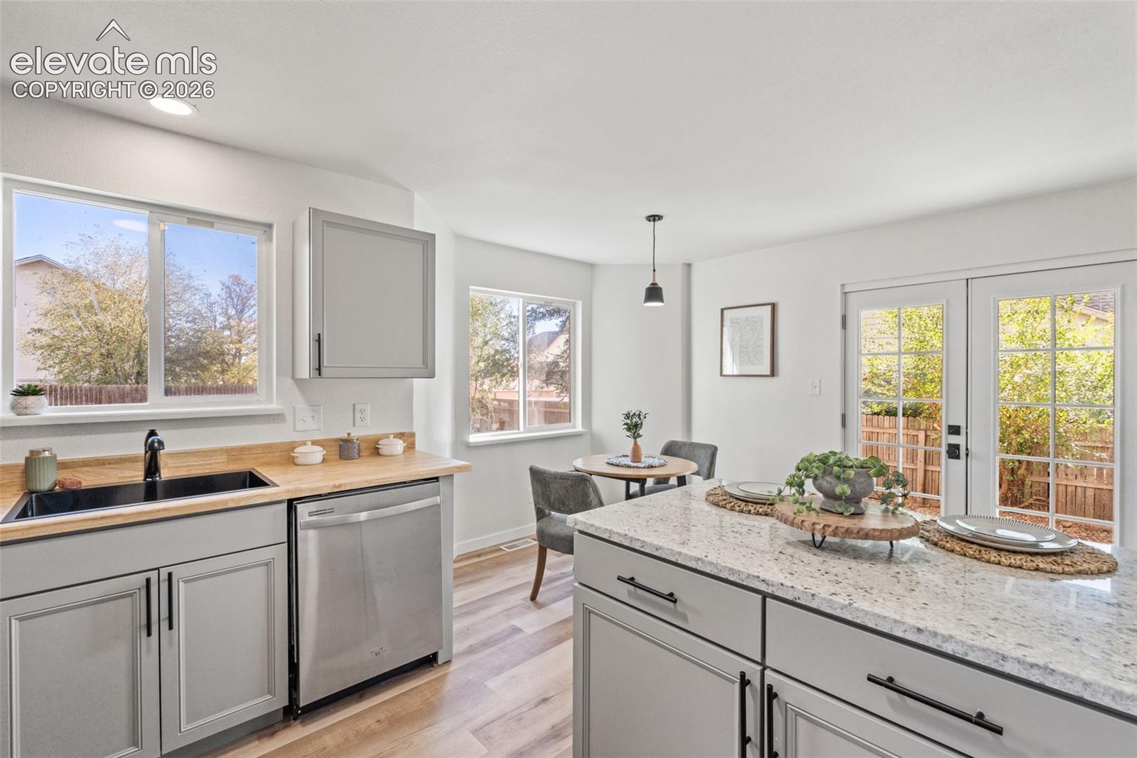 Kitchen featuring light gray shaker-style cabinetry, stone-finish countertops, wood-finish flooring, stainless steel dishwasher, and French doors