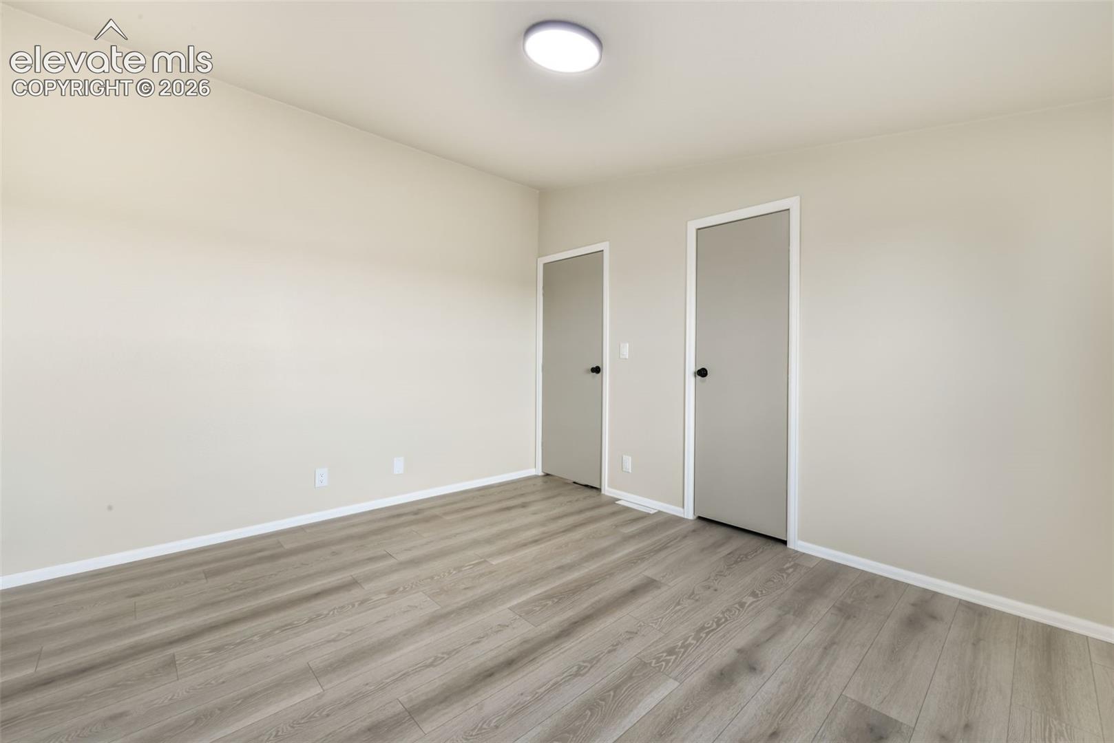 Wood-finish flooring, light neutral wall paint, two interior doors with black hardware, and an overhead flush-mount light fixture