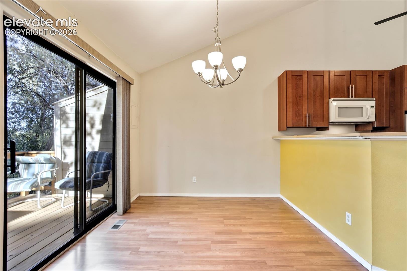 Vaulted ceiling featuring a central five-light chandelier, wood-finish flooring, sliding glass doors, and upper wood-finish cabinetry