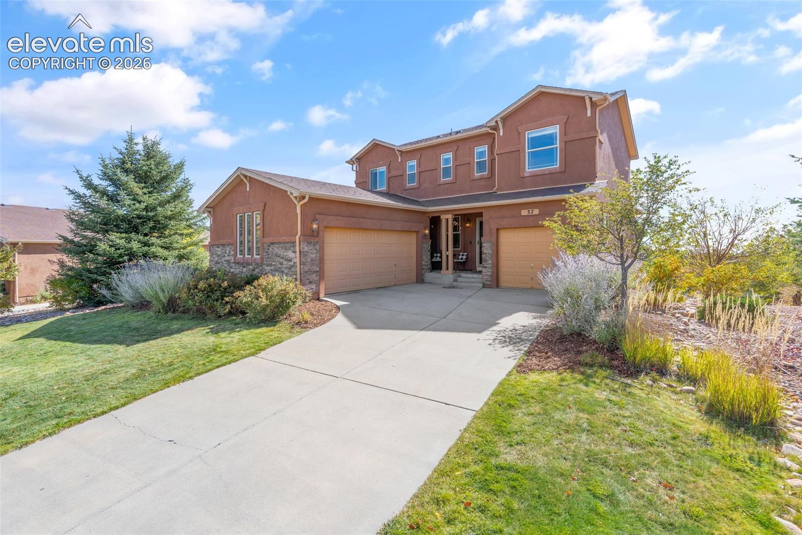 Two-story stucco exterior featuring stone veneer accents, multi-pane windows, dual attached garages, and a concrete driveway