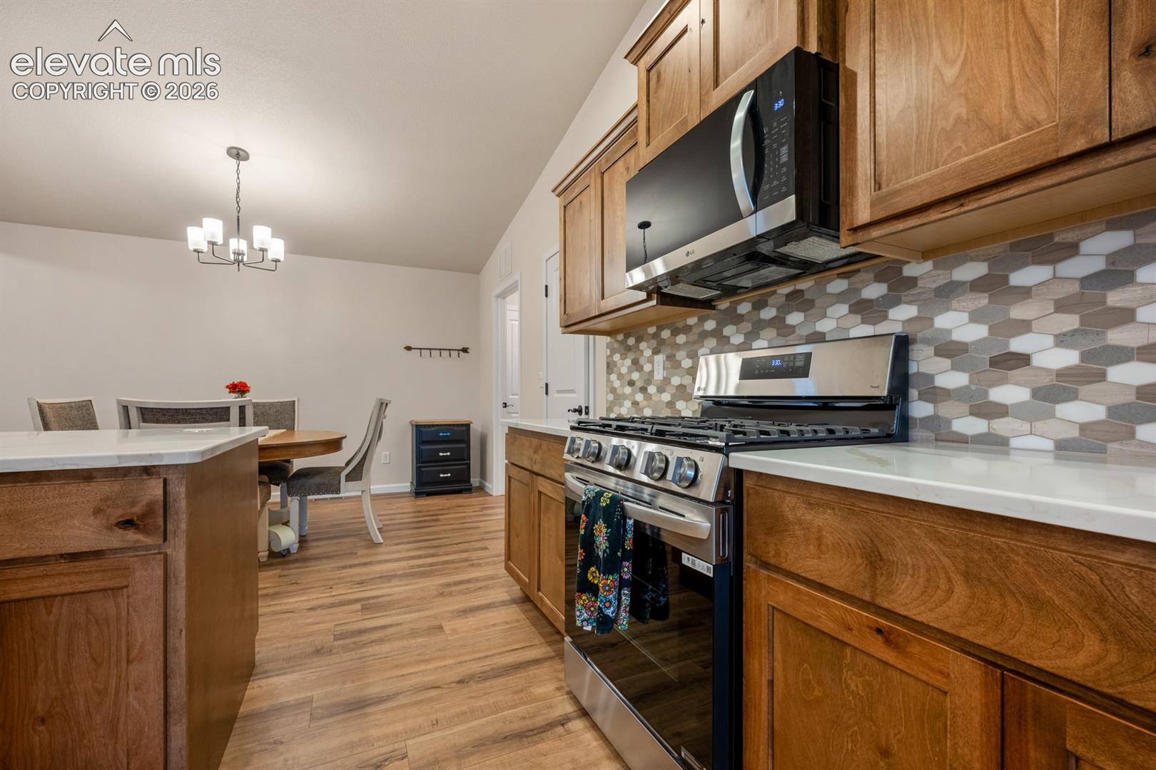 Kitchen featuring wood cabinetry, stainless steel gas range, over-the-range microwave, solid-surface countertops, and a multi-toned hexagon tile backsplash