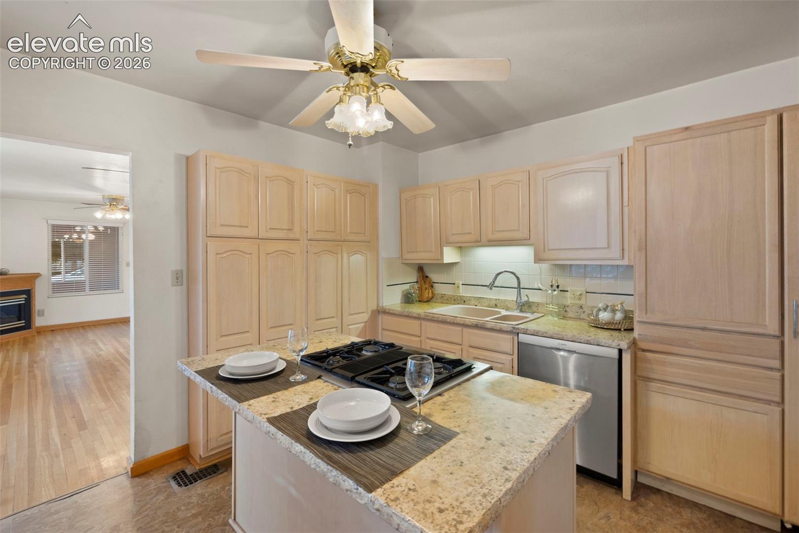Kitchen featuring a built-in gas cooktop on an island, light wood-finish cabinetry, stainless steel dishwasher, and a double basin sink