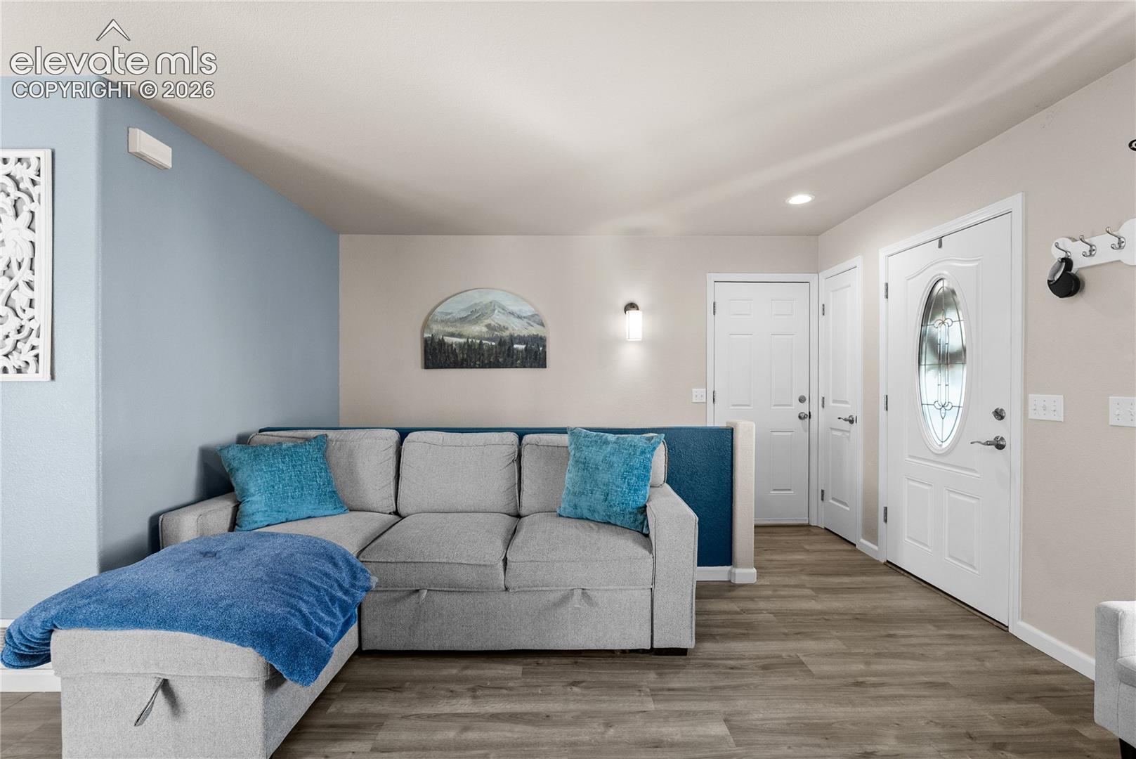 Wood-finish flooring throughout, featuring a white paneled entry door with an oval glass insert, recessed lighting, and a modern wall sconce