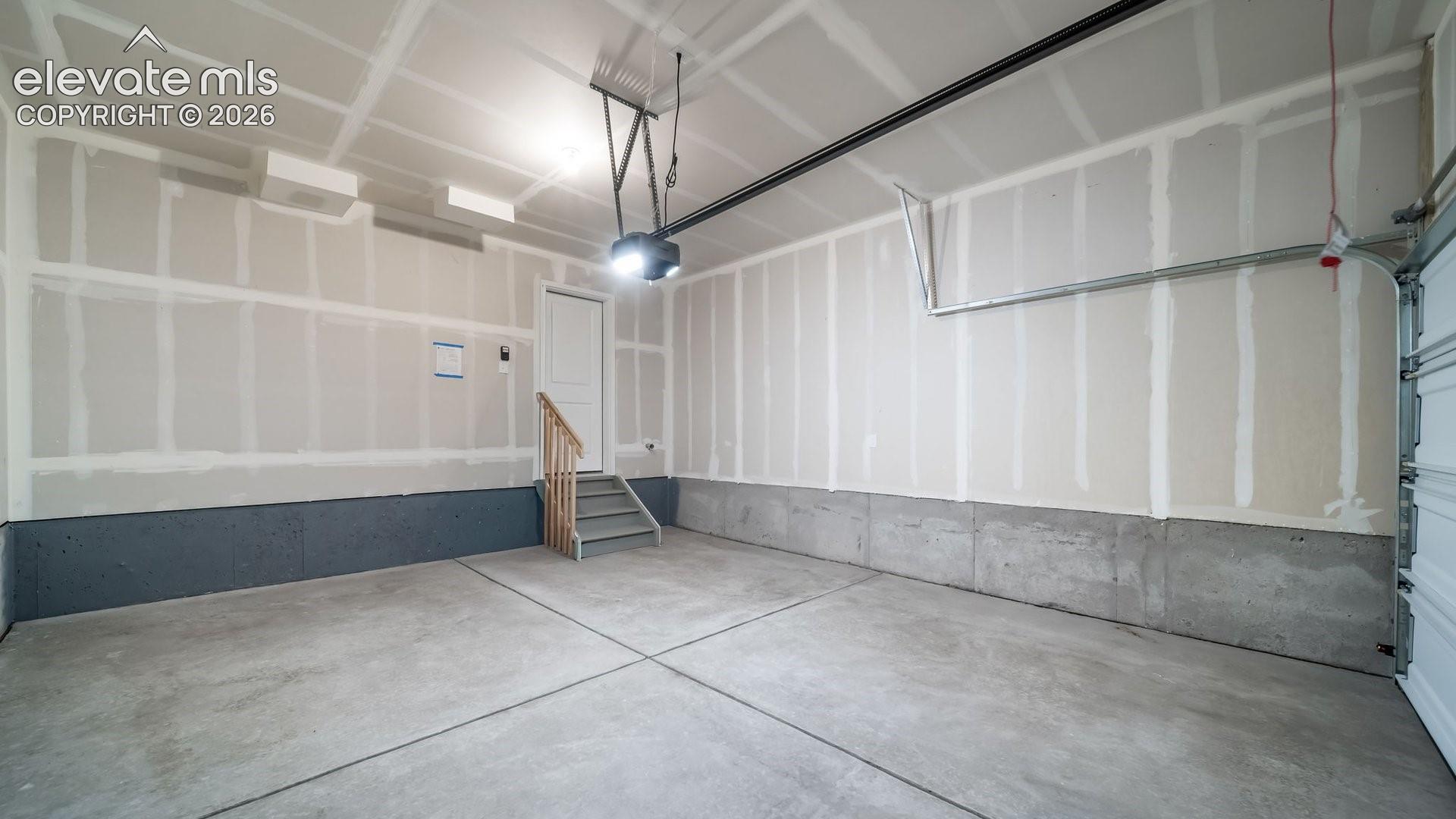 Attached two-car garage featuring a concrete floor, finished drywall, overhead door opener, and a wooden staircase with railing
*photos of a model home*