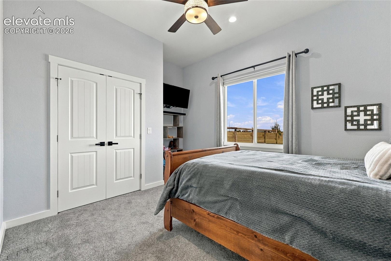Bedroom featuring high ceilings, neutral wall tones, wall-to-wall carpeting, a ceiling fan with integrated lighting, and double-panel closet doors with matte black hardware