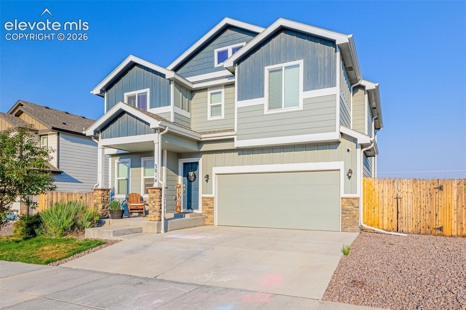 Two-story residence featuring a covered front porch with stone-clad columns, an attached two-car garage, and a wood privacy fence