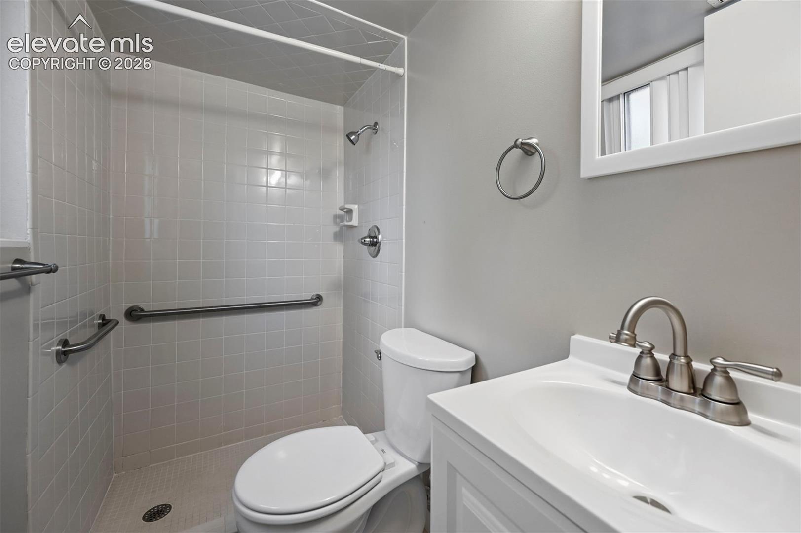 Walk-in shower with white square tiles and grab bars