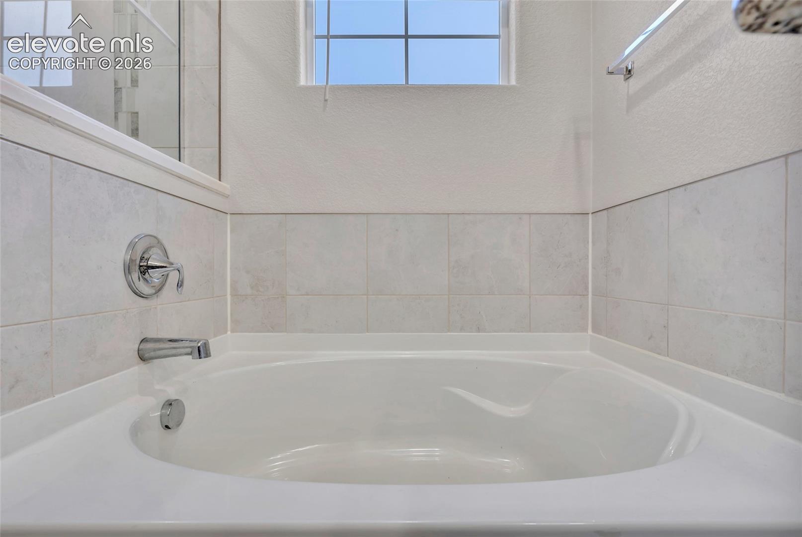 Built-in soaking tub with chrome fixtures, tiled surround, and a clear glass shower enclosure