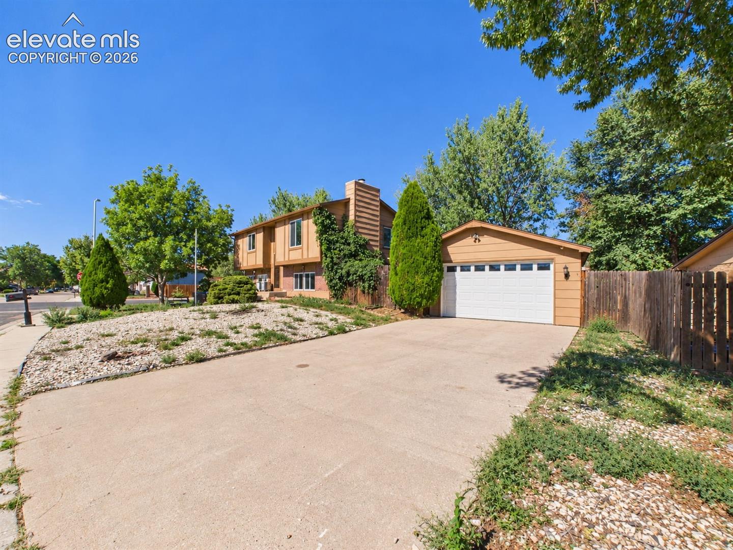 Split-level exterior features a broad driveway, mature landscaping, and multiple access points at the front of the home.
