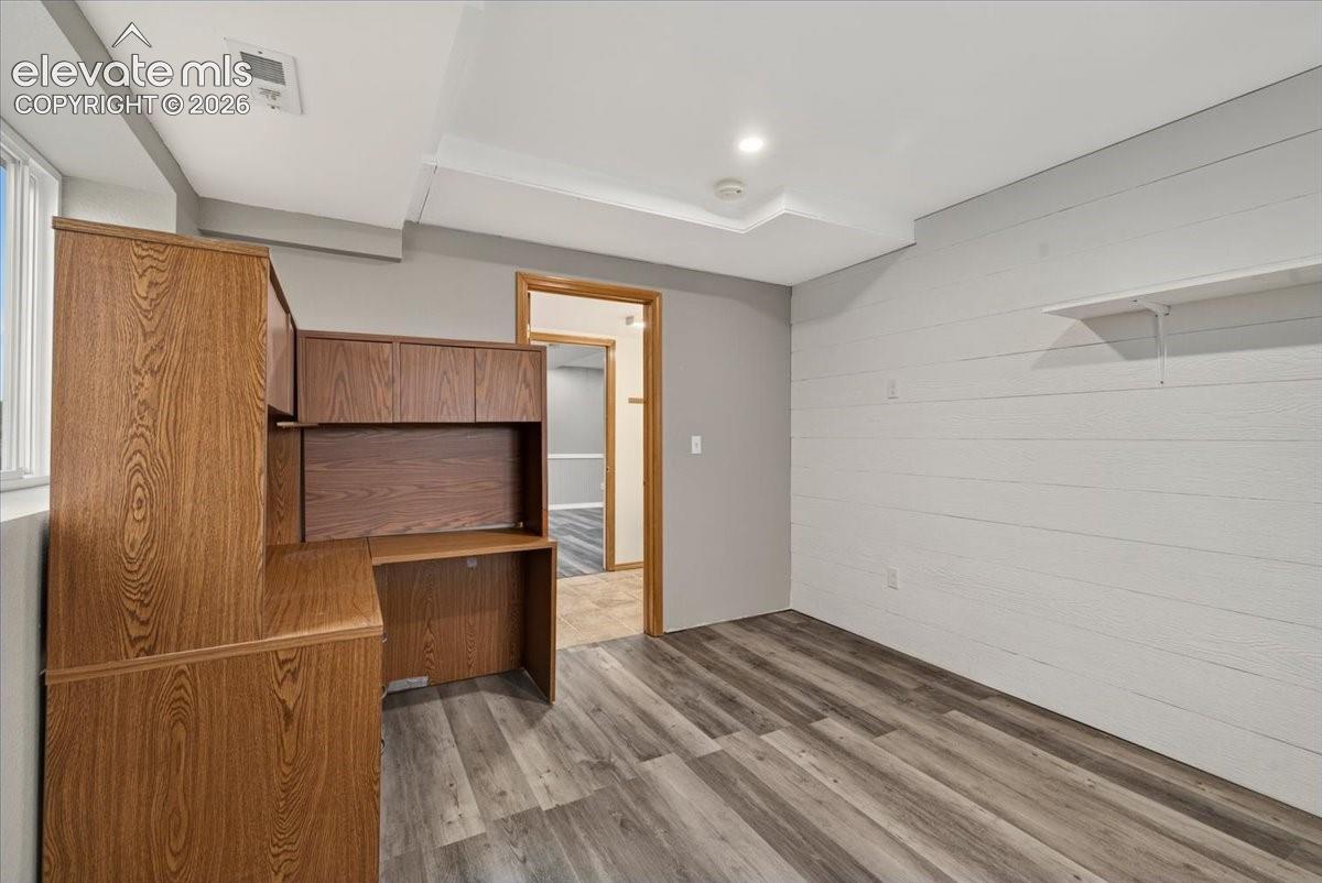 Wood-finish flooring, horizontal plank wall detailing, built-in wooden cabinetry, and a wall-mounted floating shelf