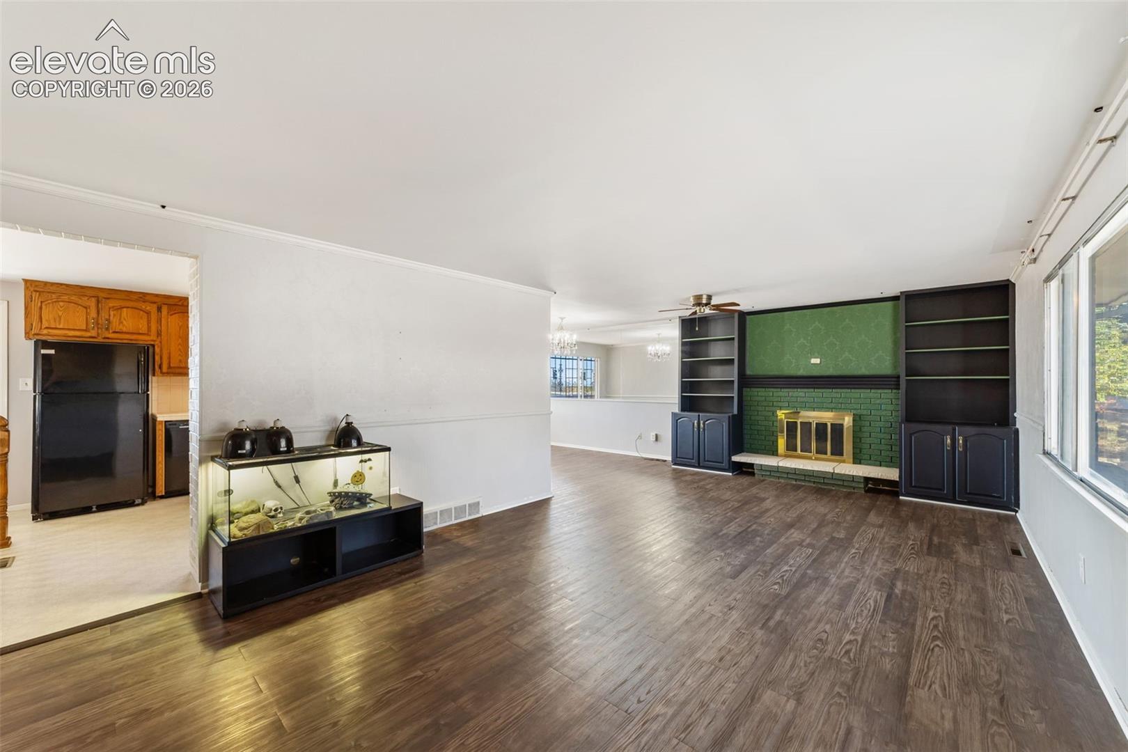 Spacious living area featuring wood-finish flooring, a prominent fireplace with a green tiled surround and brass insert, and built-in shelving units