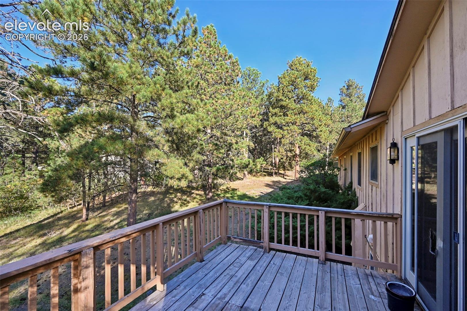 Wood deck with wood railing, sliding glass door, exterior wall lantern, and board and batten siding