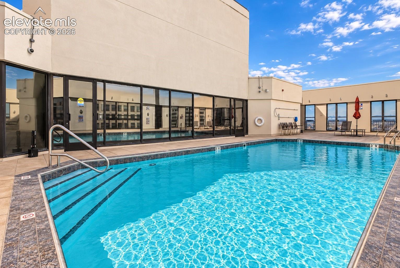 Outdoor swimming pool with integrated steps, surrounded by tile decking and a glass-enclosed building facade