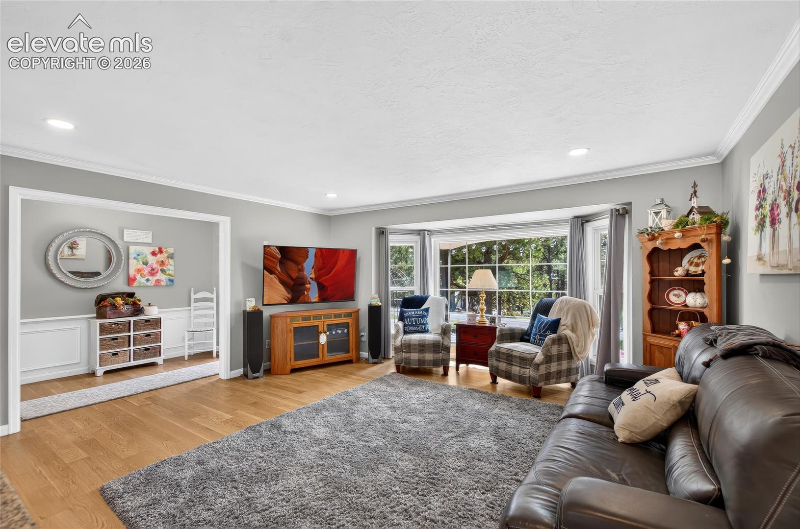 Expansive living area featuring a large bay window, recessed lighting, crown molding, and wood-finish flooring