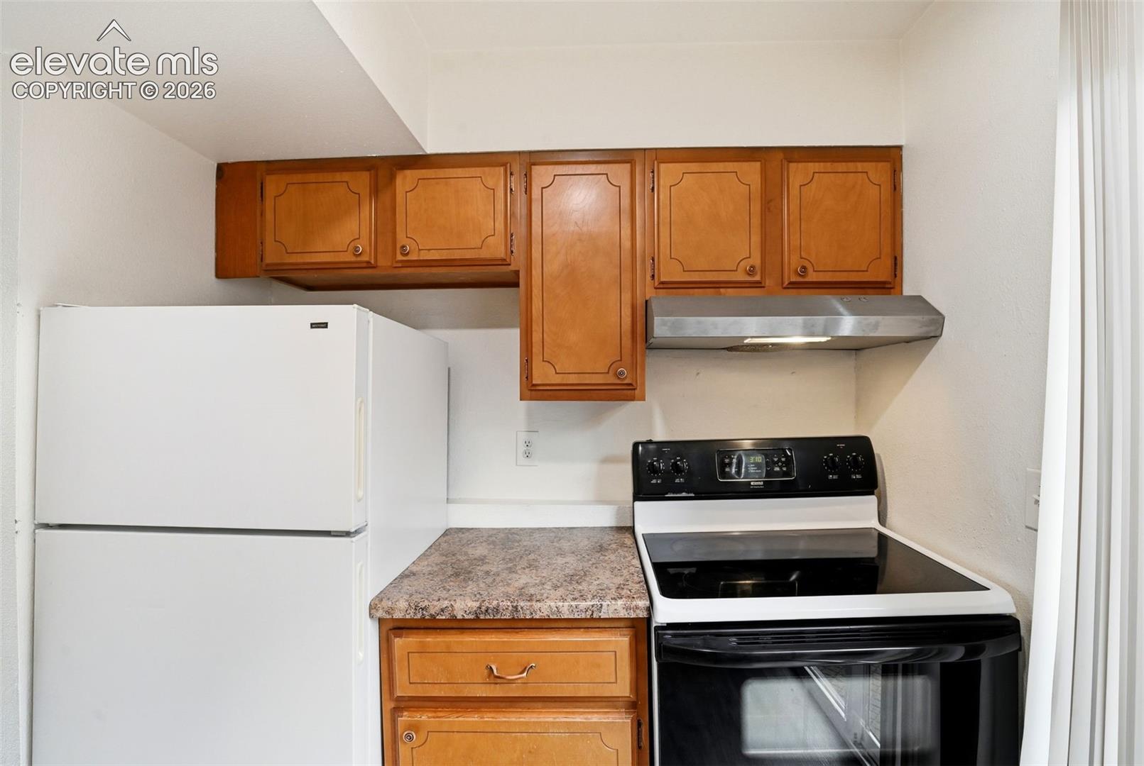 Wood-finish cabinetry, built-in range hood, white refrigerator, and black electric range