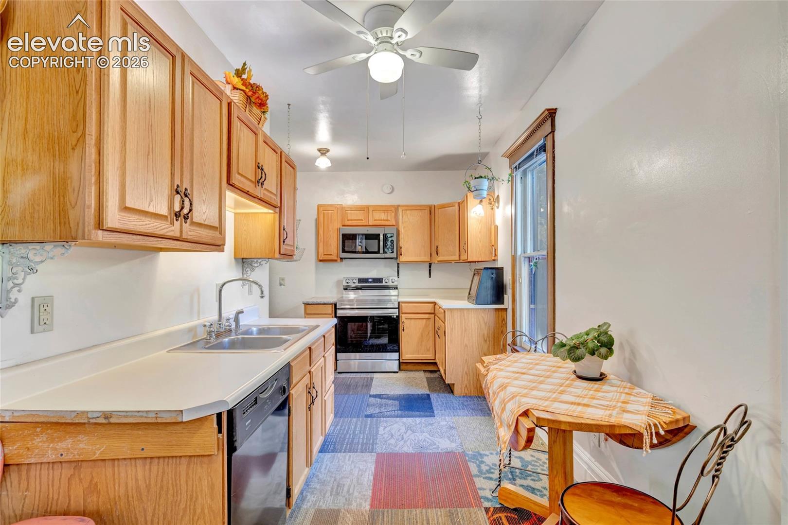 Kitchen featuring wood cabinetry, stainless steel appliances, dual-basin sink, and a ceiling fan
