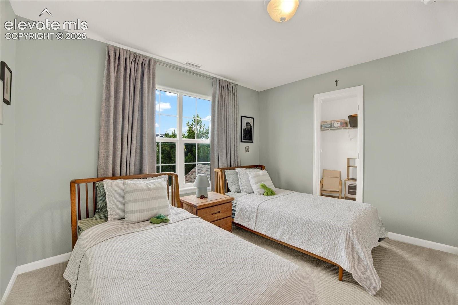 Neutral-toned bedroom featuring wall-to-wall carpeting, a multi-pane window with natural light, and a built-in walk-in closet