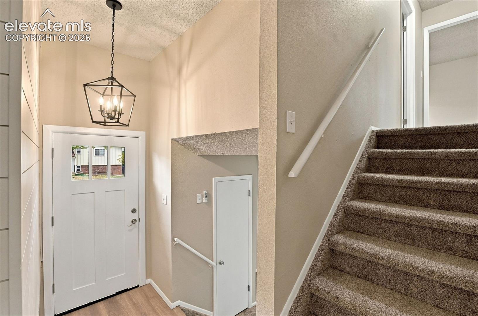 Entryway featuring a white exterior door with window inserts, a geometric metal pendant light fixture, wood-finish flooring, and carpeted stairs with a white handrail