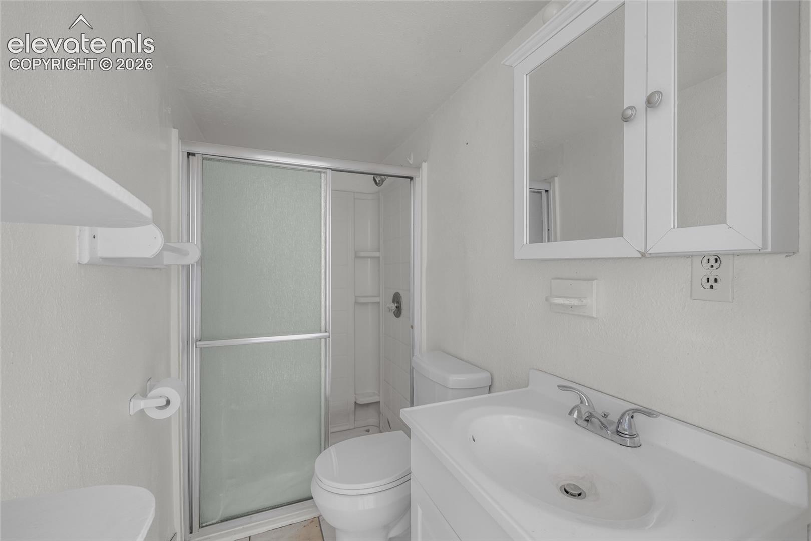 Bathroom featuring a shower stall with sliding frosted glass doors, white vanity with integrated sink, chrome faucet, and a wall-mounted medicine cabinet
