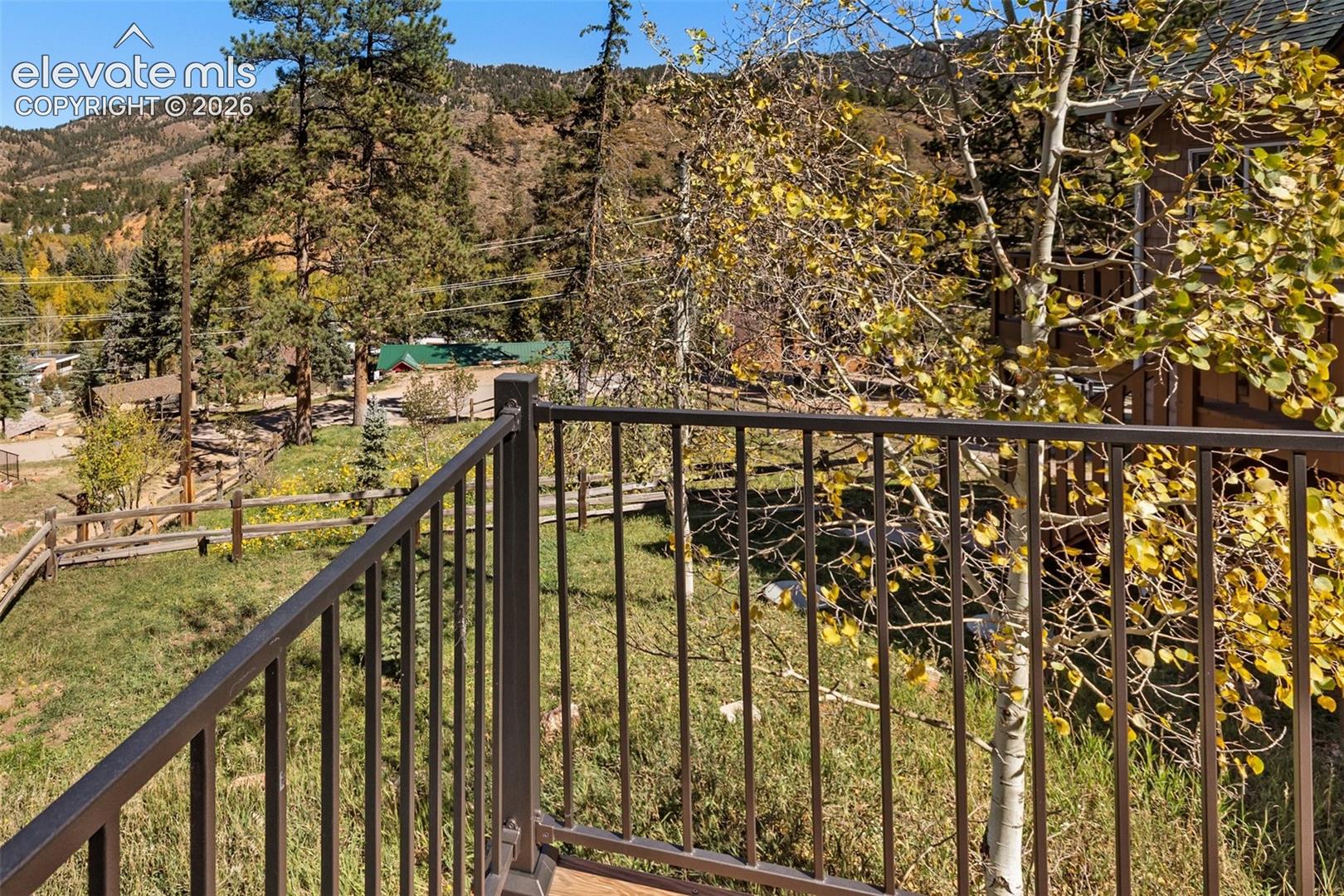Elevated balcony featuring a dark metal railing, natural landscape, mature trees, and mountain terrain backdrop