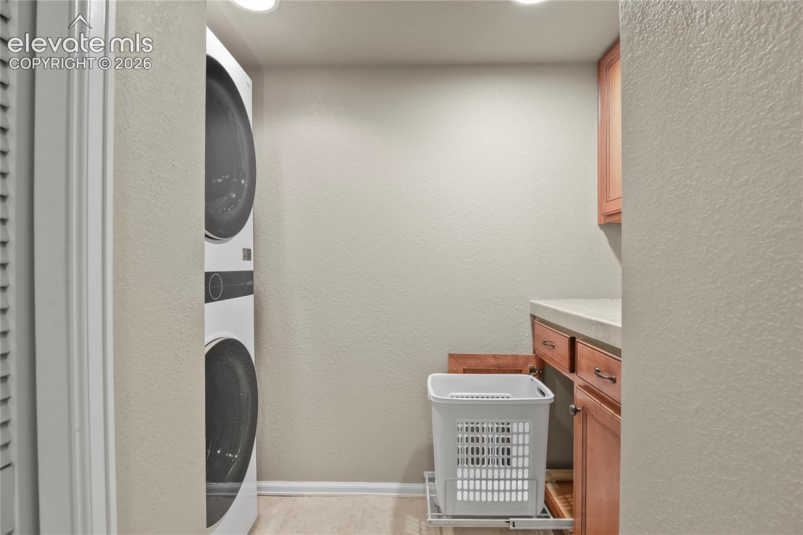 Utility area featuring a stacked laundry appliance, wooden cabinetry, stone-surface countertop, and two pull-out hamper drawers