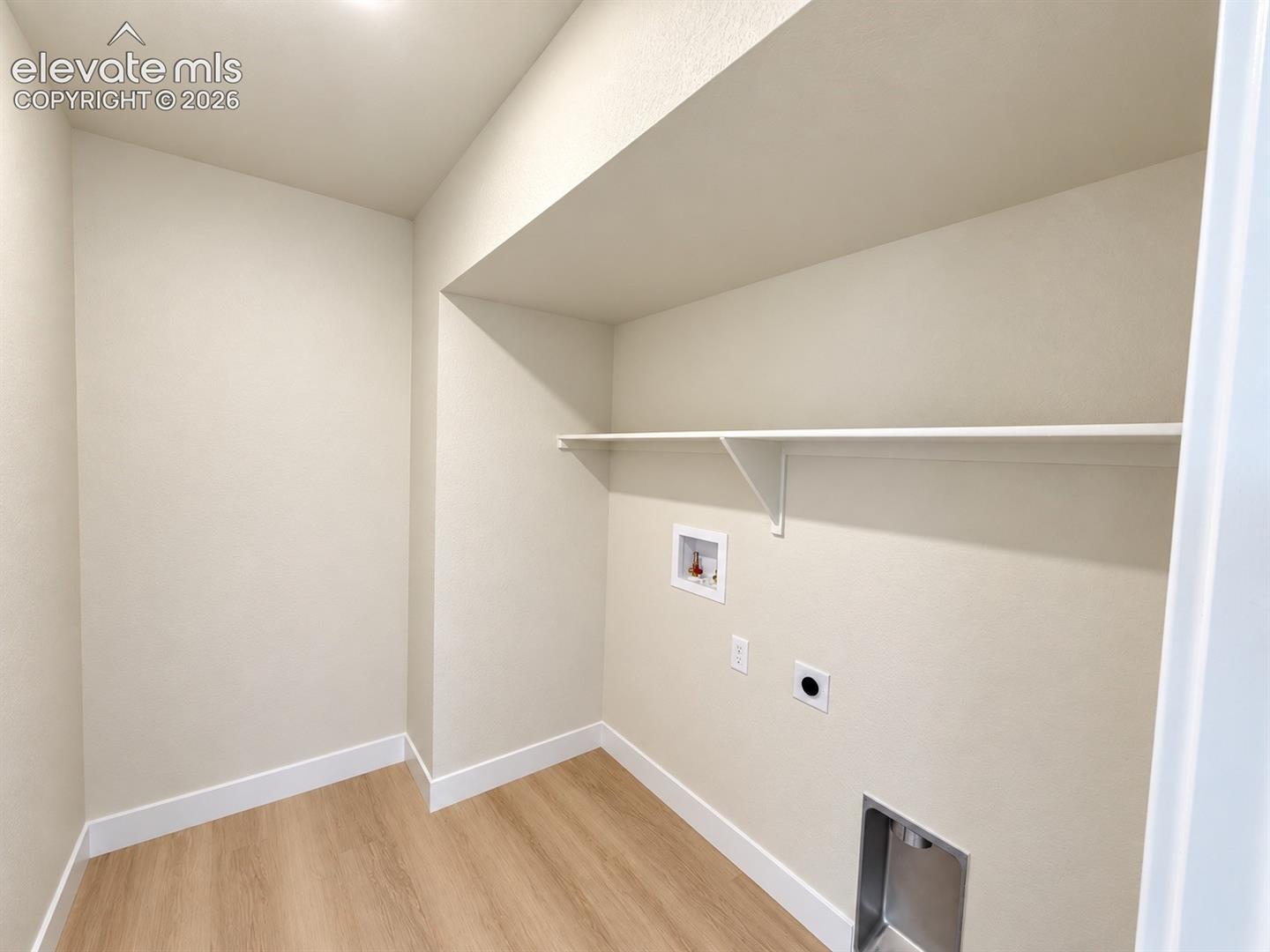 Utility area featuring wood-finish flooring, a built-in recessed shelf, and dedicated water and electrical hookups