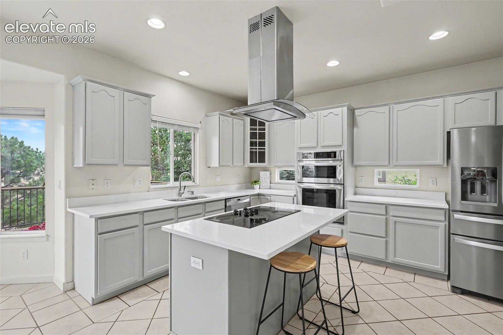 Contemporary kitchen featuring light gray cabinetry, white countertops, stainless steel appliances, and a central island with an integrated cooktop