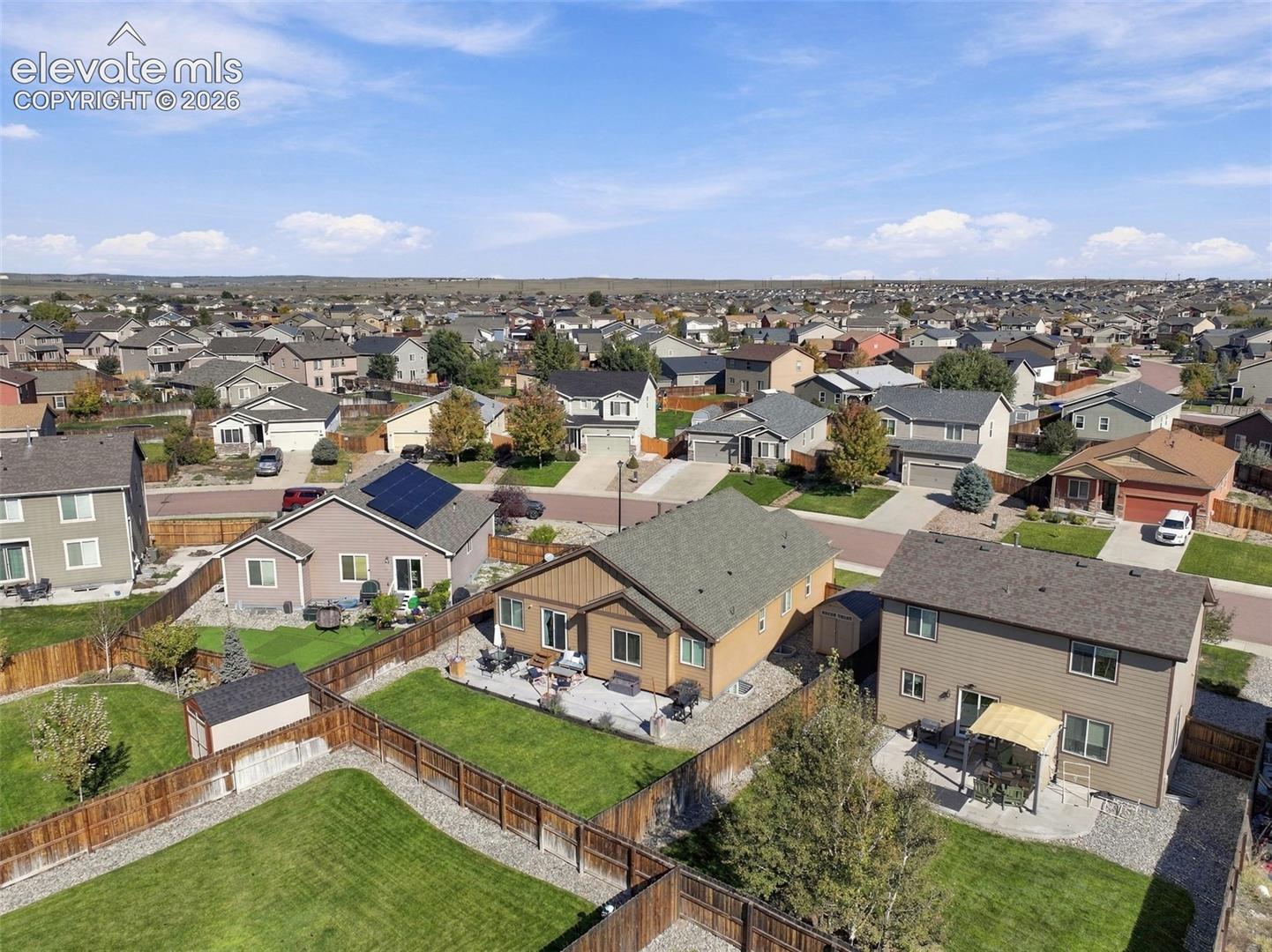 Aerial perspective featuring residential lots with fenced backyards, manicured lawns, concrete patios, and solar panels