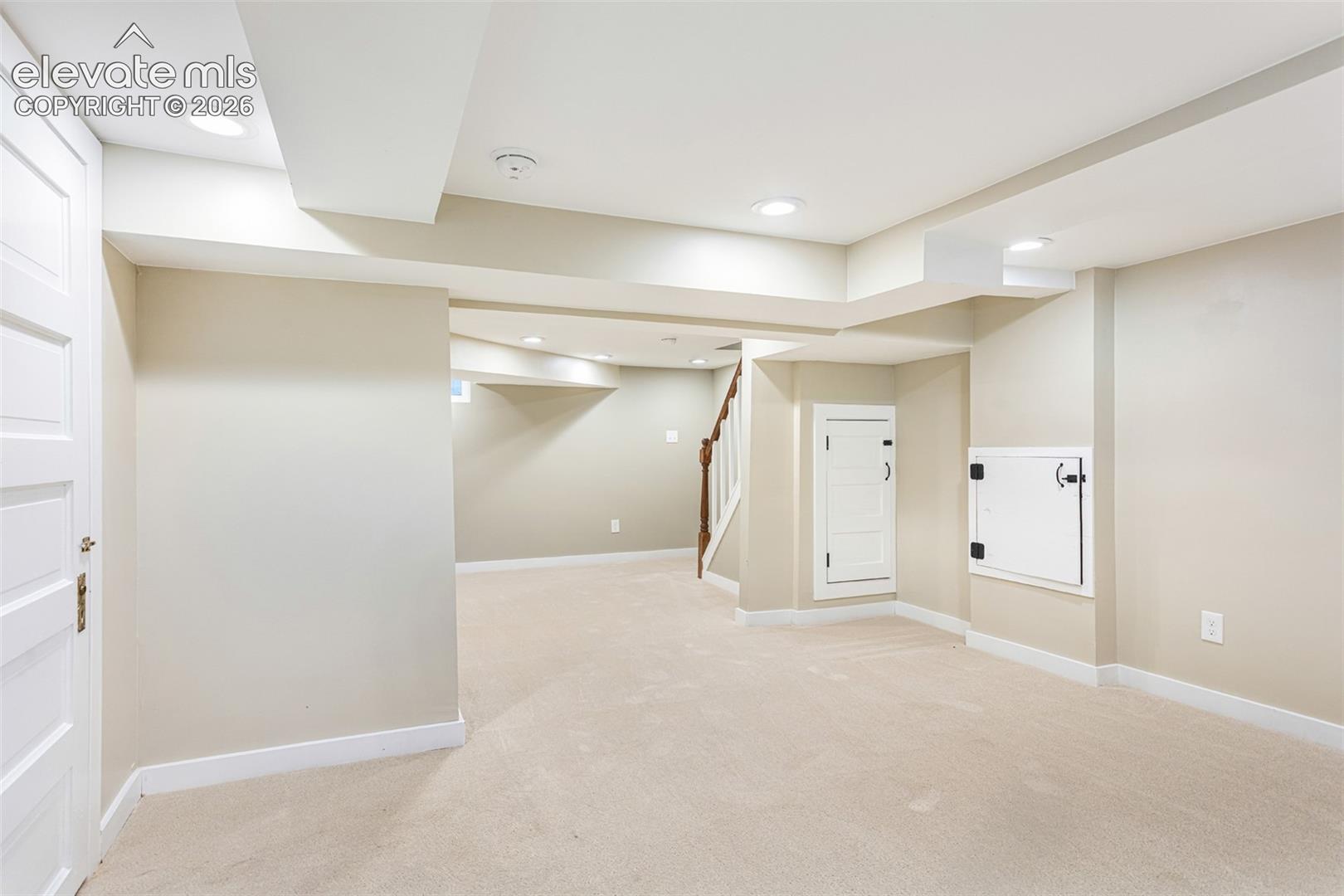 Spacious carpeted room featuring recessed lighting, painted walls, white trim, and a visible staircase with a wood handrail