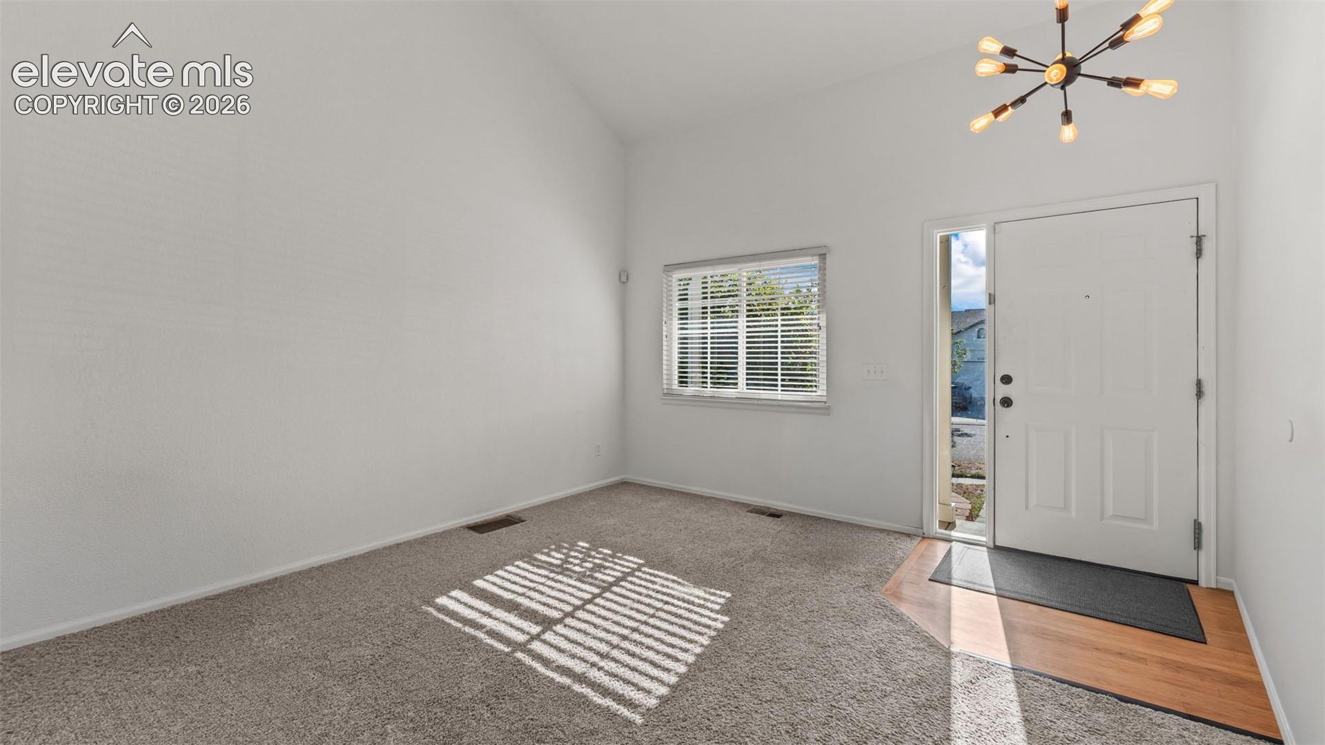 Vaulted ceiling, contemporary chandelier, front entry door with sidelight, wood-finish flooring, and carpet