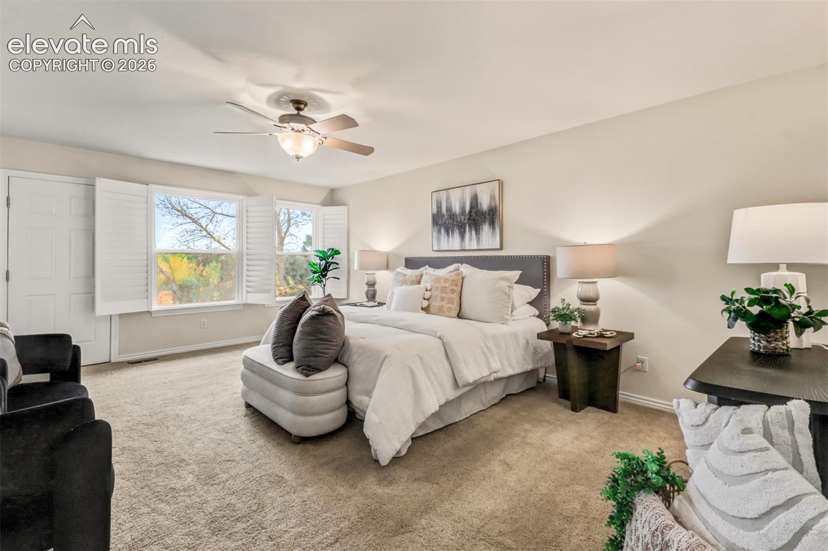 Carpeted room featuring dual-panel interior doors, plantation shutters, and a ceiling-mounted light fixture with fan