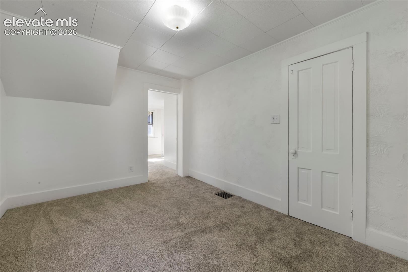 Room featuring neutral wall-to-wall carpeting, textured wall finish, and a classic four-panel interior door with white trim