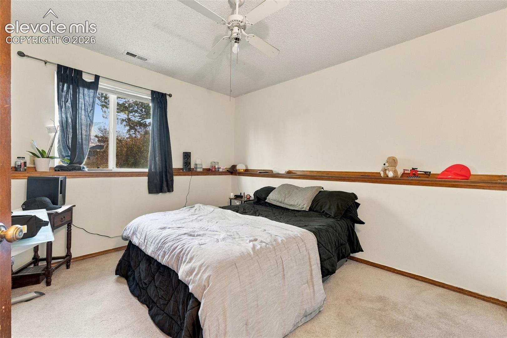 Bedroom featuring neutral carpeting, a central ceiling fan, and a built-in wooden chair rail shelf