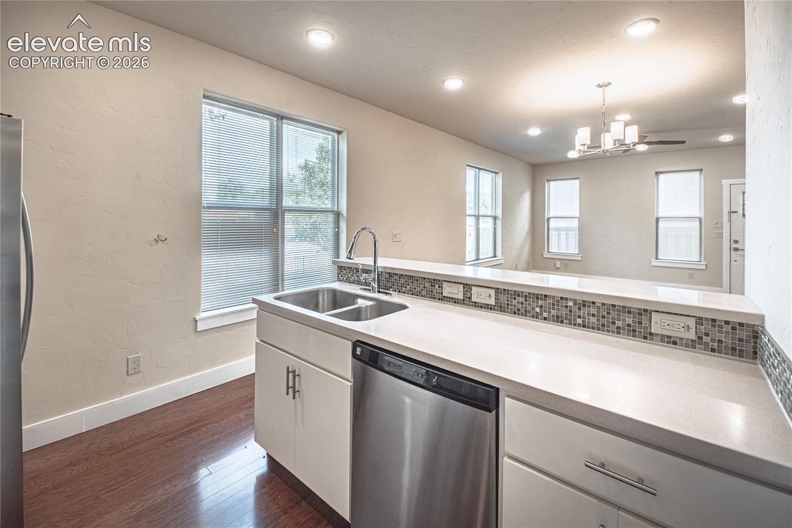 Kitchen featuring a stainless steel double sink with gooseneck faucet, light-toned countertops, tile backsplash, and wood-finish flooring