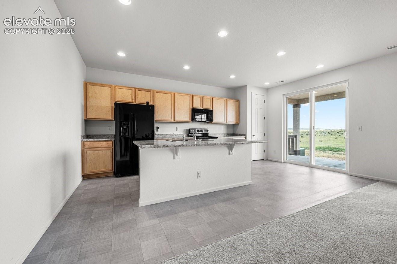Kitchen with wood cabinetry, black appliances, a central island with a granite countertop, and recessed lighting