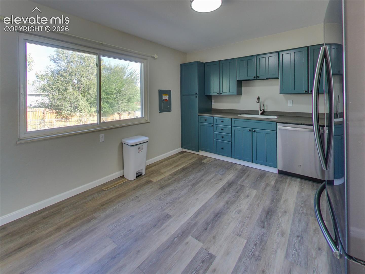 Kitchen space featuring teal cabinetry, dark countertops, a stainless steel refrigerator, a stainless steel dishwasher, and wood-finish flooring