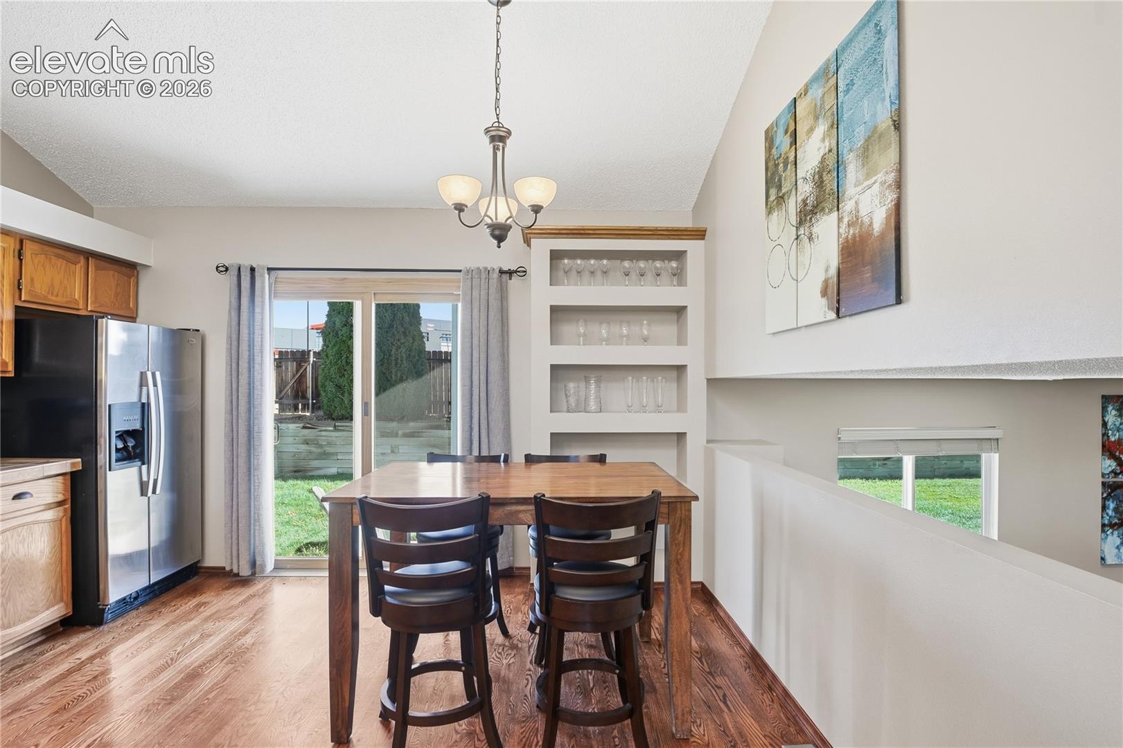 DINING AREA FEATURING VAULTED CEILINGS, WOOD-FINISH FLOORING, A BUILT-IN RECESSED SHELVING UNIT, AND A SLIDING GLASS DOOR PROVIDING WITH WALK-OUT TO BACKYARD