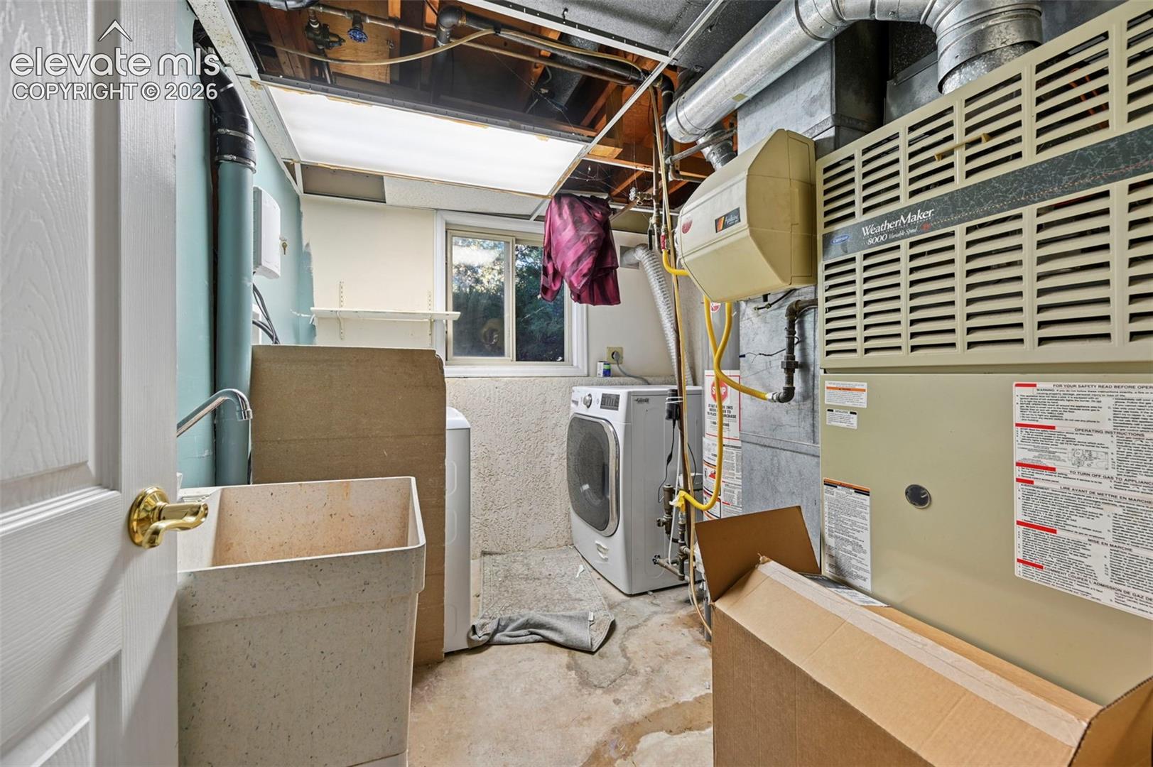 Utility room featuring a laundry sink with a faucet, a window, exposed ceiling joists, and a furnace with ductwork