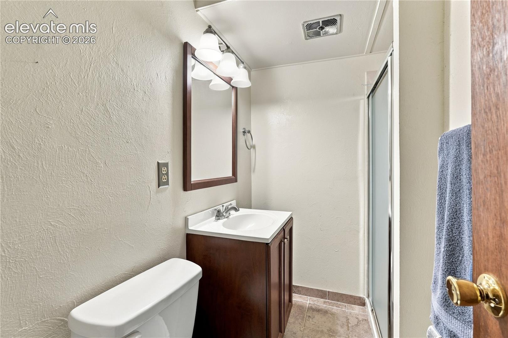 Bathroom featuring a wood-tone vanity cabinet with a white basin, a wall-mounted mirror with a wood frame, a three-light fixture, and a glass-enclosed shower stall