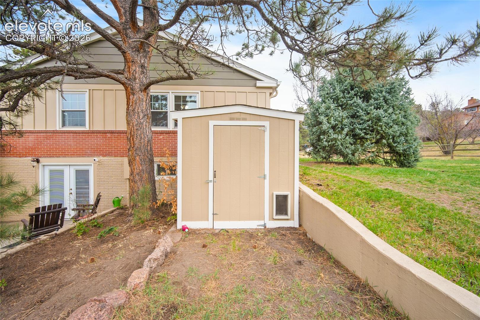 Exterior storage shed with a tan finish, complemented by a concrete retaining wall and brick and panel siding foundation