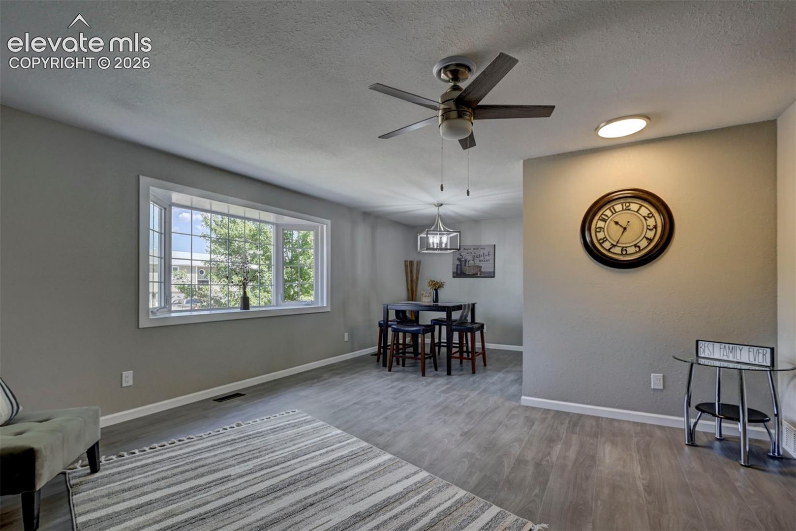 Large bay window, wood-finish flooring, ceiling fan with integrated lighting, and contemporary pendant lighting